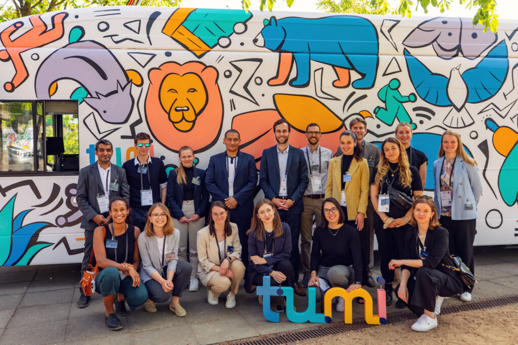 group picture of 17 people (11 women, 6 men) in front of an e-bus painted with brightly coloured animal shapes.