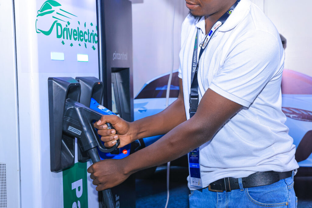 A man in a white t-shirt is plugging an electric vehicle charging cable into a charging station.