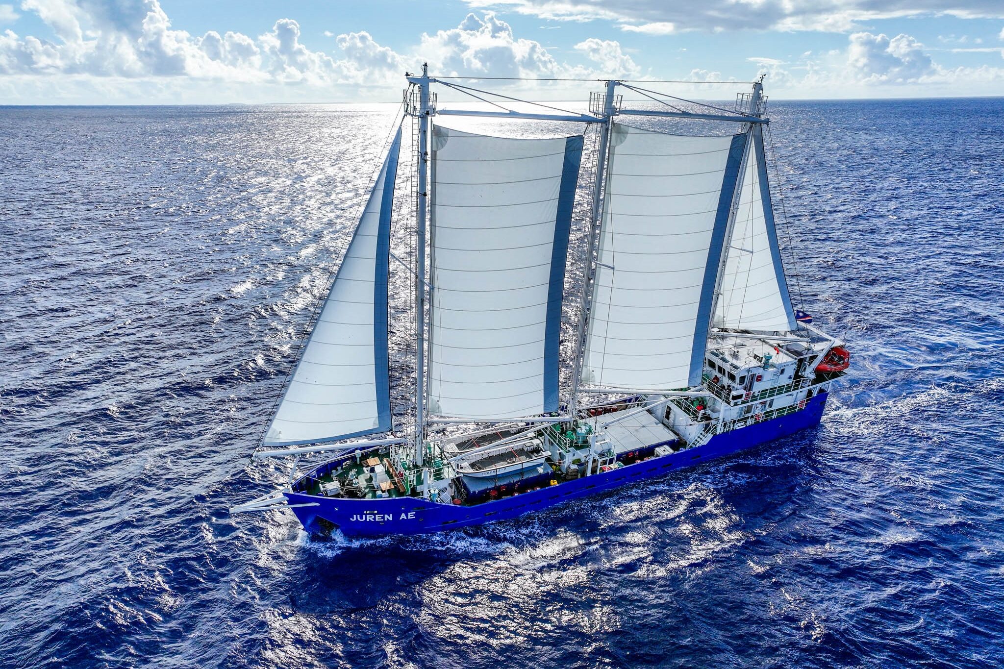The cargo sailing ship SV Juren Ae out on open water with a slightly cloudy sky above.