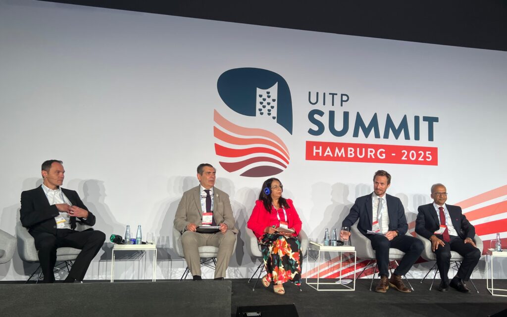 Four mean and one women sitting in a panel on stage with a UITP Summit Hamburg 2025 banner in the background.